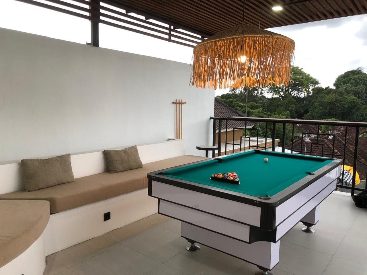 Covered deck with pool table, cushioned bench and treetop views