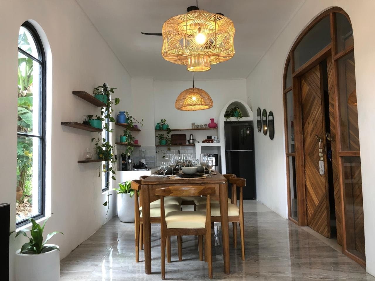 Dining table for six under woven pendant lights, with the kitchen and arched doors beyond