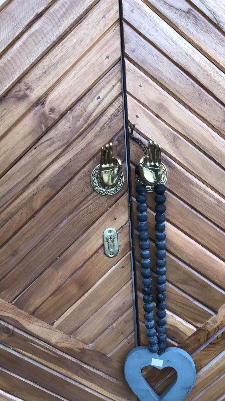 Teak door with brass handles and a blue beaded heart tassel