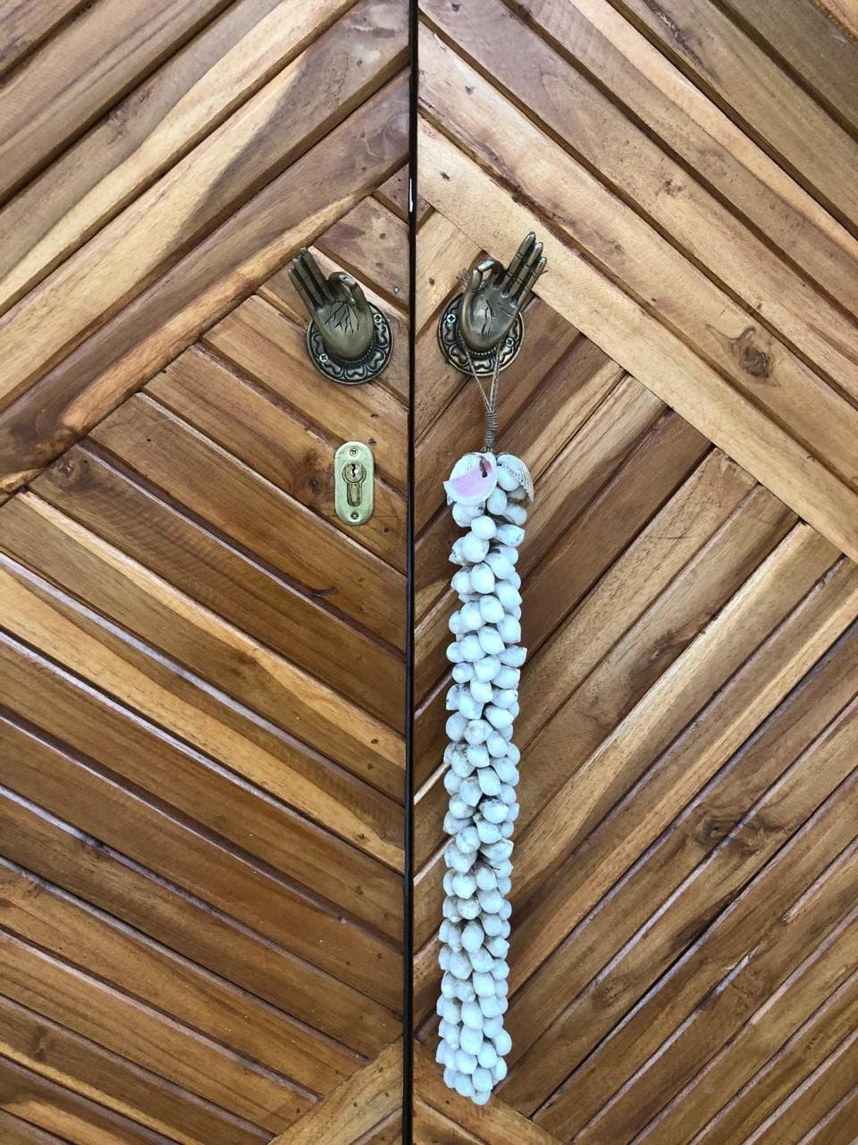 Teak door with brass hand handles and a white shell tassel