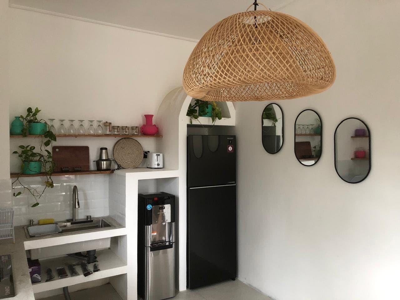 Kitchen with fridge, water dispenser, sink and a woven pendant light