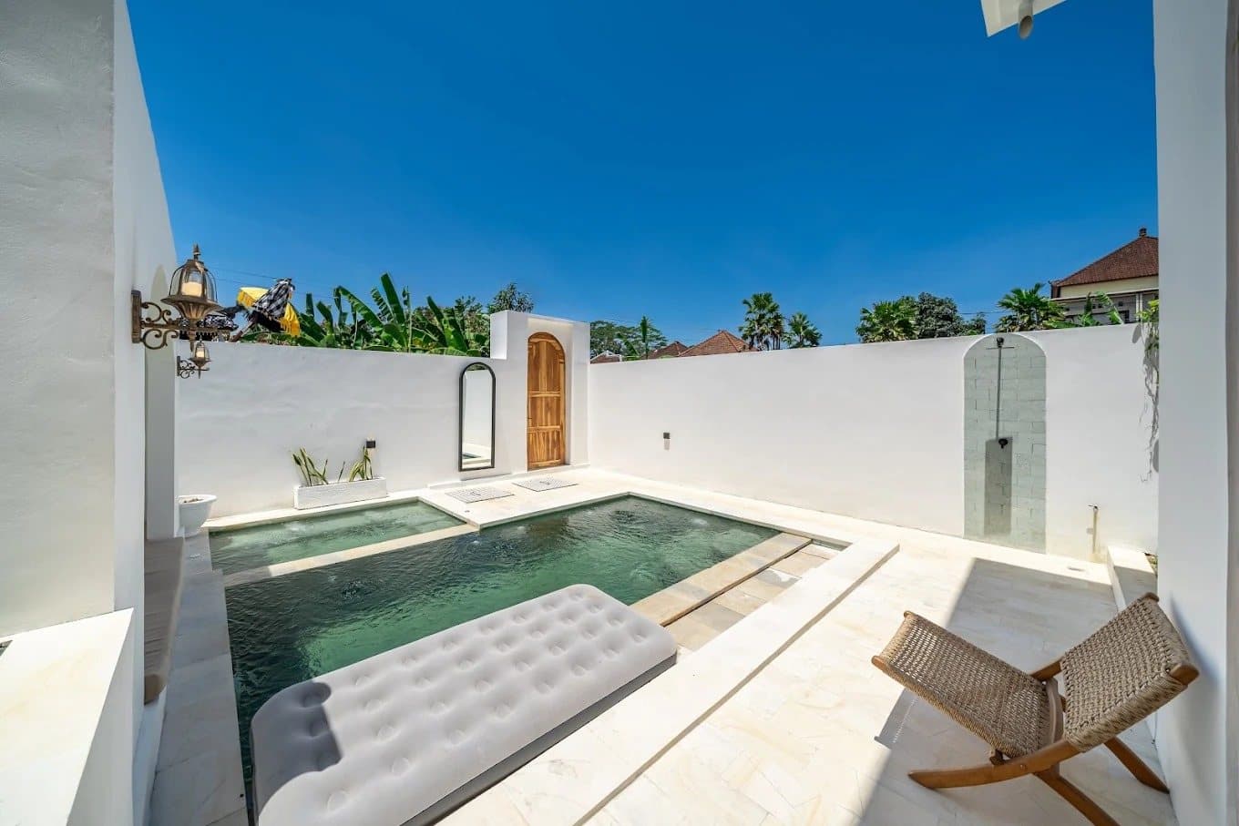 Private pool with sun lounger beside a white garden wall and banana trees