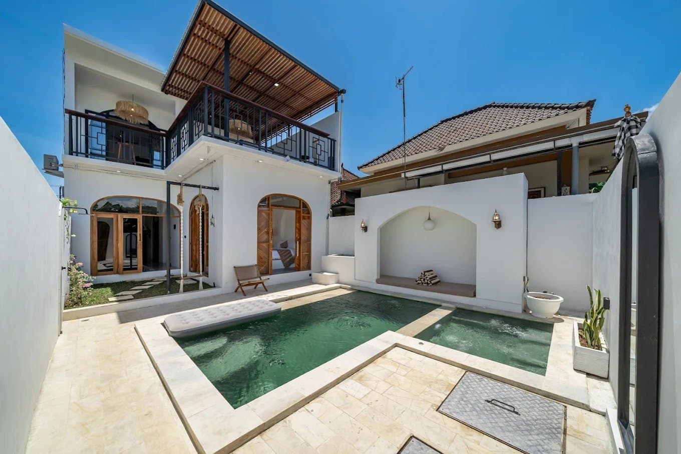 Two-story white villa with arched teak doors behind a private pool